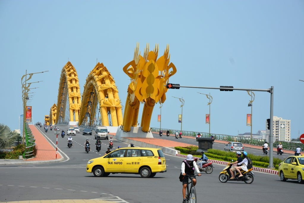 Drachenbrücke Da Nang am Tag. Auf den sechs Spuren Autos, Mopeds und auf dem Mittelstreifen der gelbe Drachen. Platz für Fußgänger ist rechts und links davon. Foto: Sandip Roy via Unsplash